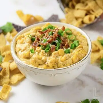 Creamy crock pot crack corn dip garnished with green onions and bacon bits.