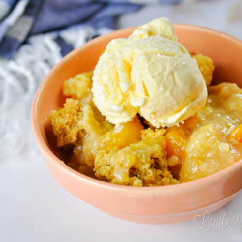bowl of peach cobbler in front of a blue striped towel.