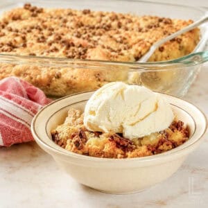 a bowl of pineapple dump cake topped with ice cream, in front of a baking dish.