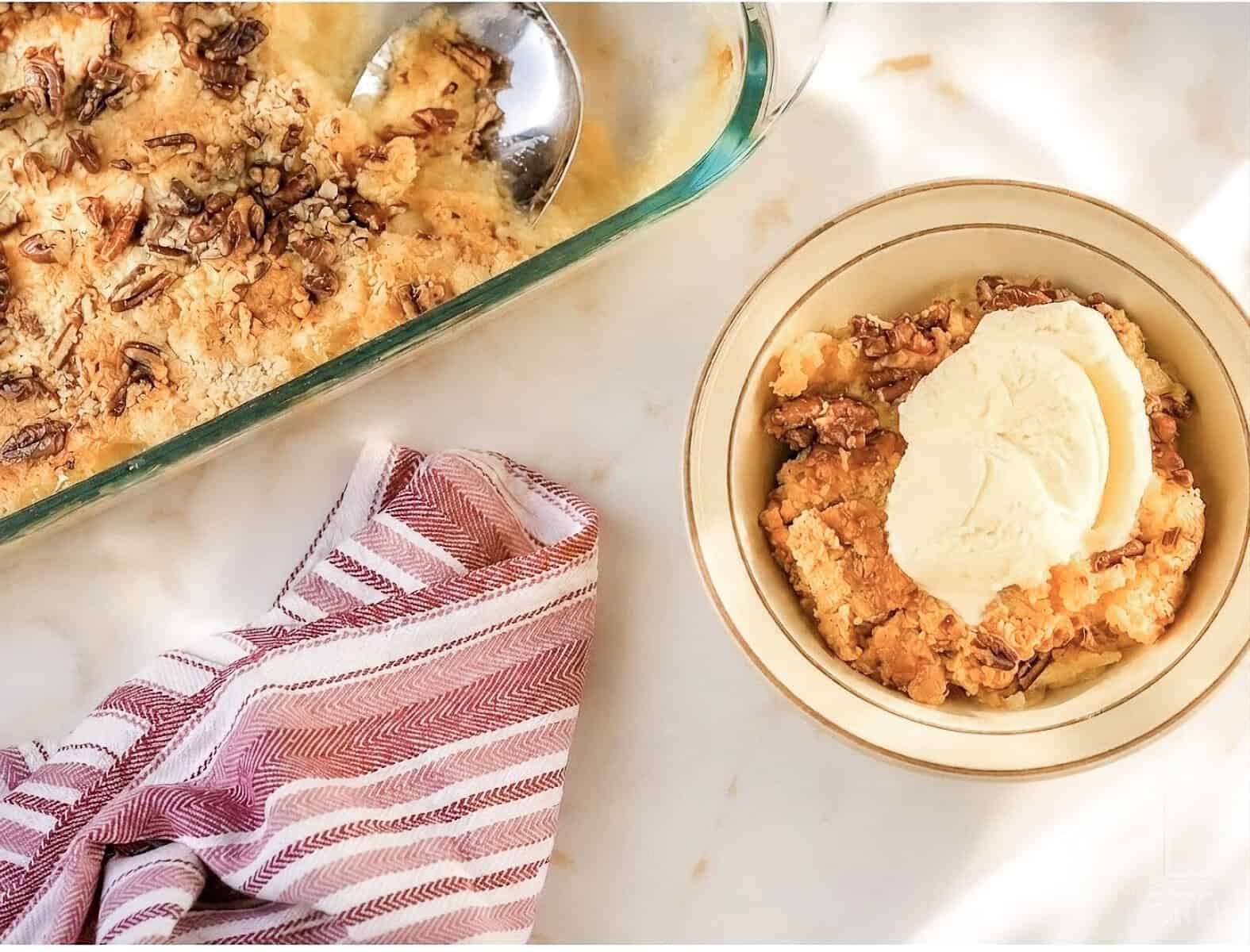 Pineapple dump cake with a scoop of vanilla ice cream in a bowl on a marble surface.