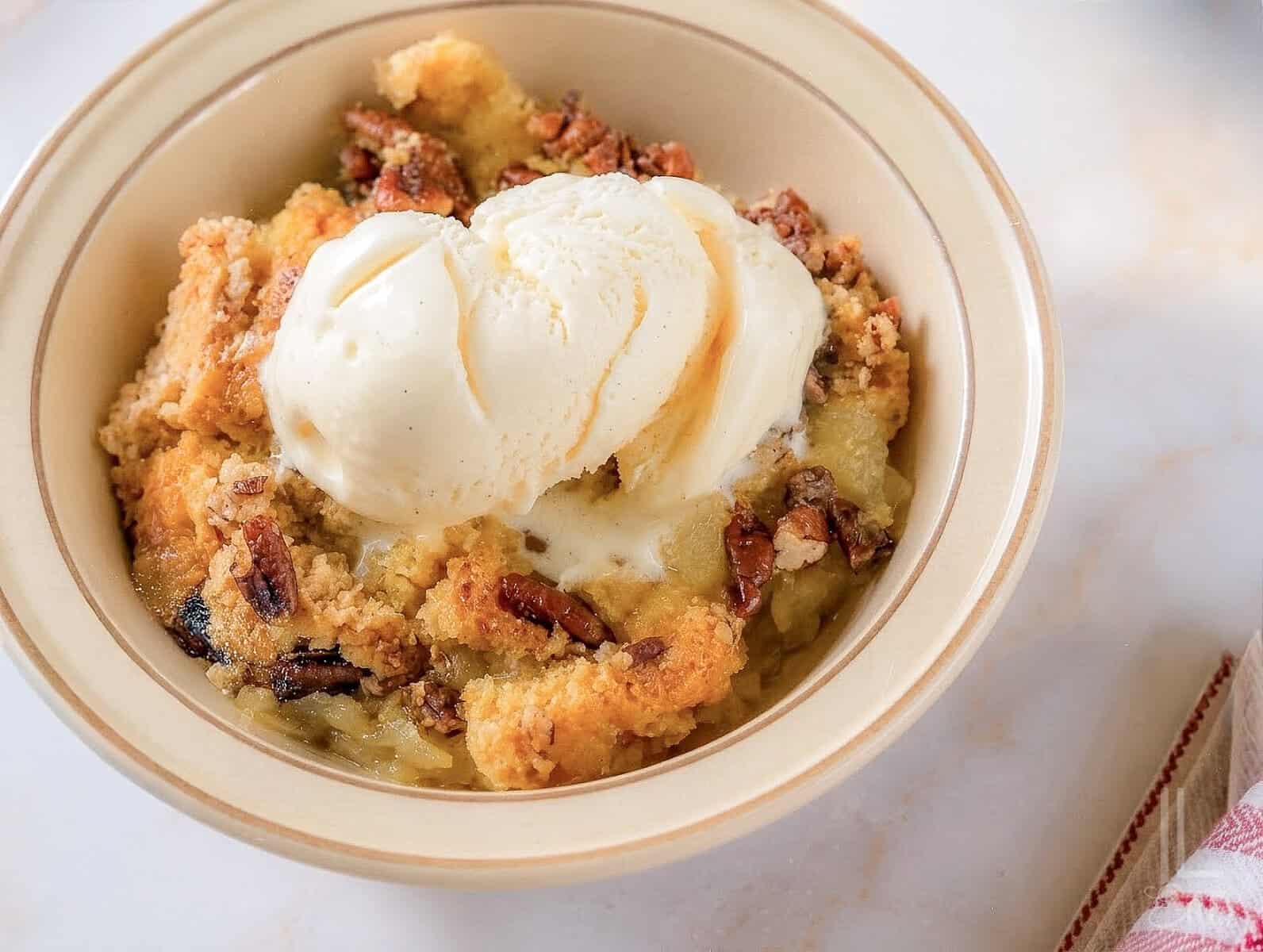 Pineapple dump cake with vanilla ice cream in a bowl, topped with ice cream.