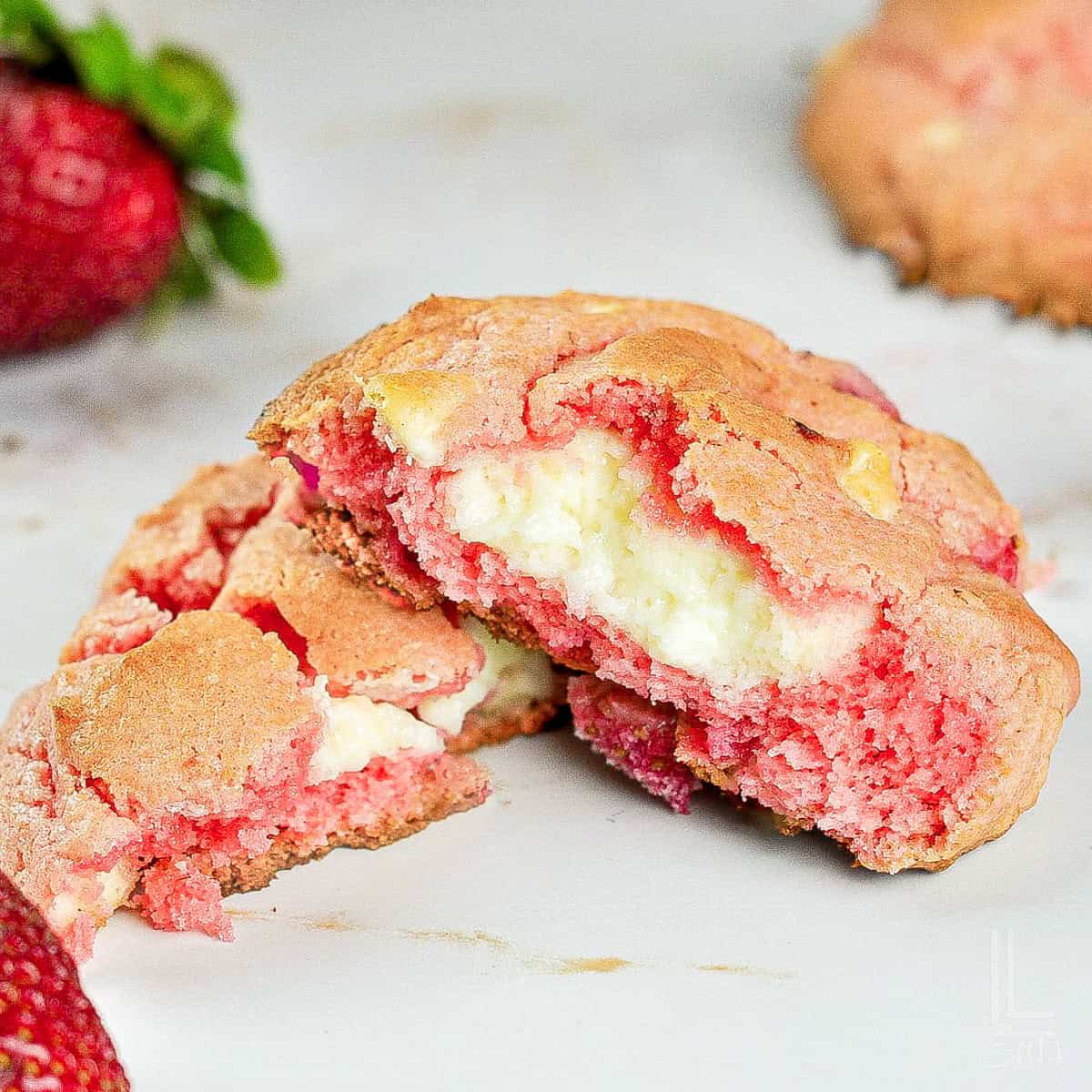 Strawberry cheesecake cookies with a cake mix outside and white cheesecake filling on a white surface.