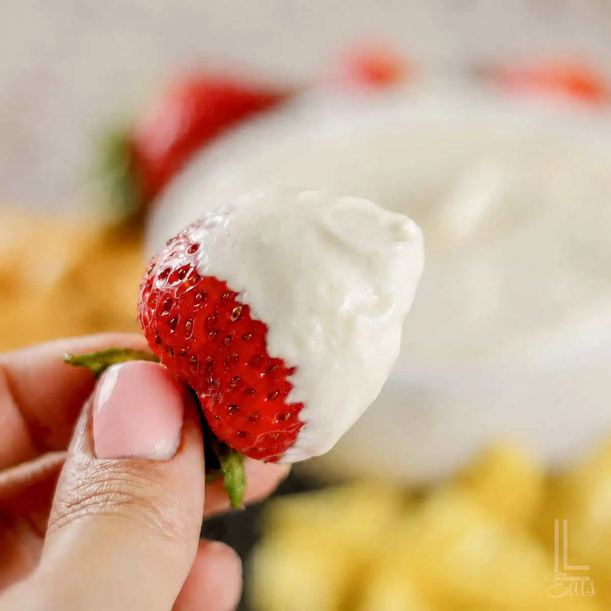 Strawberry dipped in sweet cream cheese dip, in front of the bowl of fruit dip.