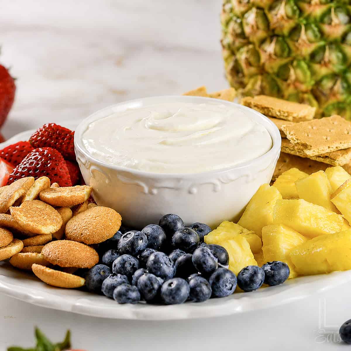 sweet cream cheese fruit dip in a bowl, surrounded by fruits and sweet crackers.