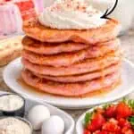Stack of strawberry cake mix pancakes with whipped cream and syrup.