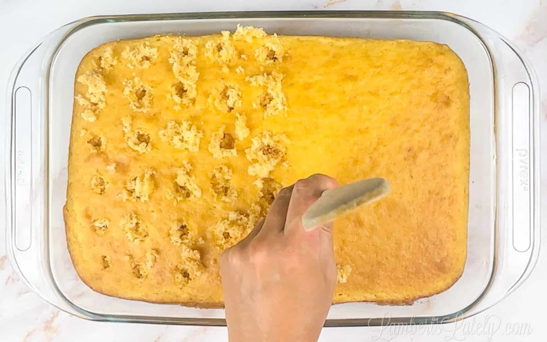 poking holes in a banana cake with a wooden spoon handle.