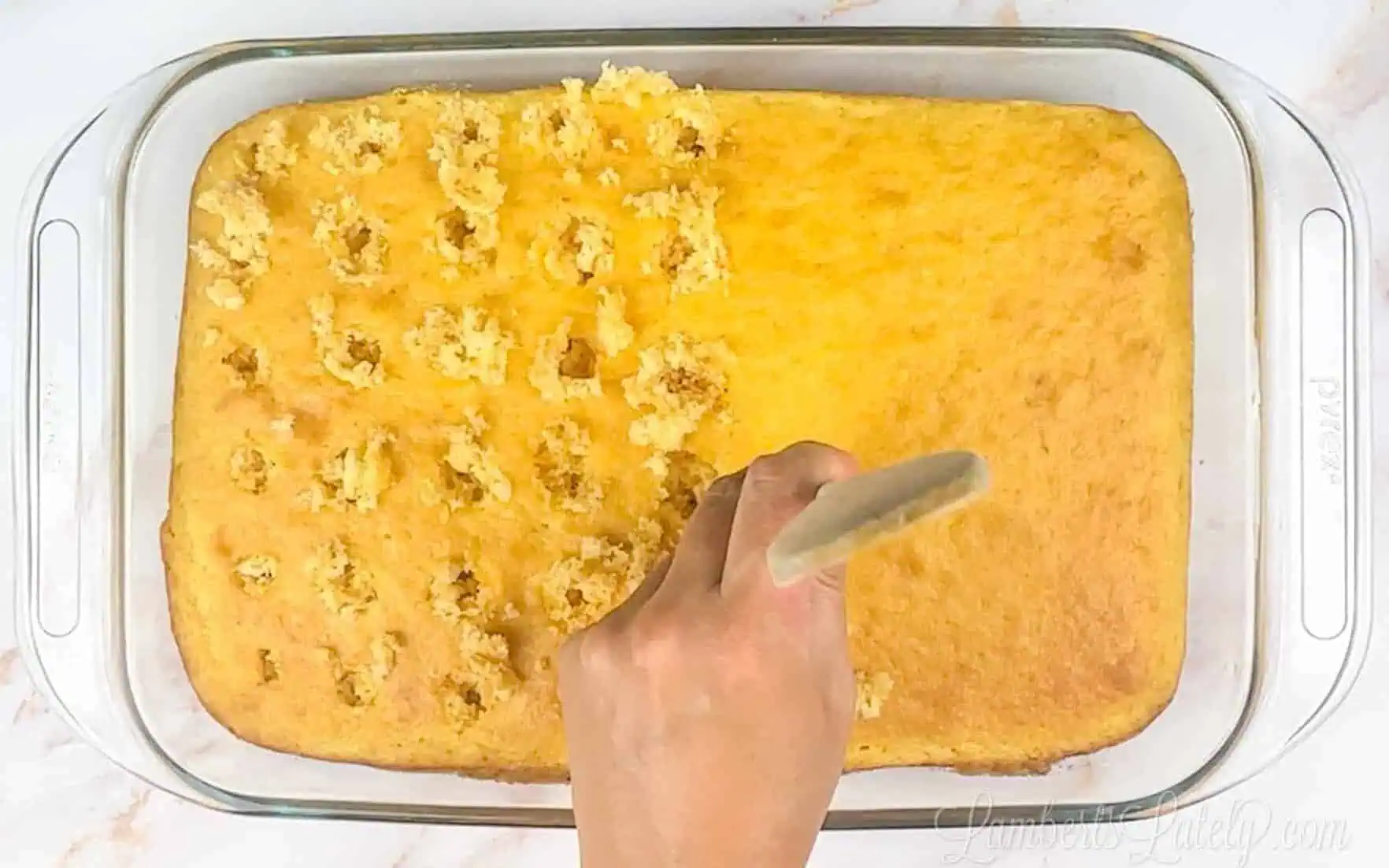 poking holes in a banana cake with a wooden spoon handle.