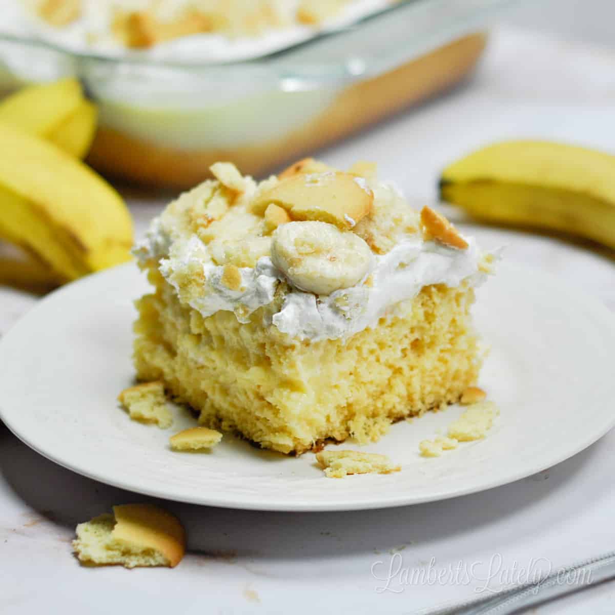 piece of banana pudding poke cake on a plate, surrounded by bananas.