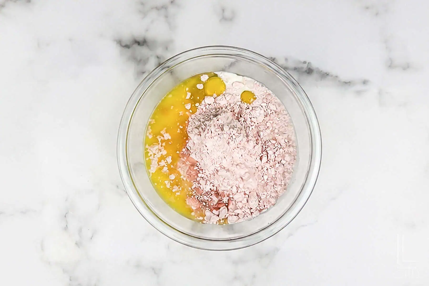 Eggs, flour, and pink cake mix in a glass bowl on marble surface for pancake batter.