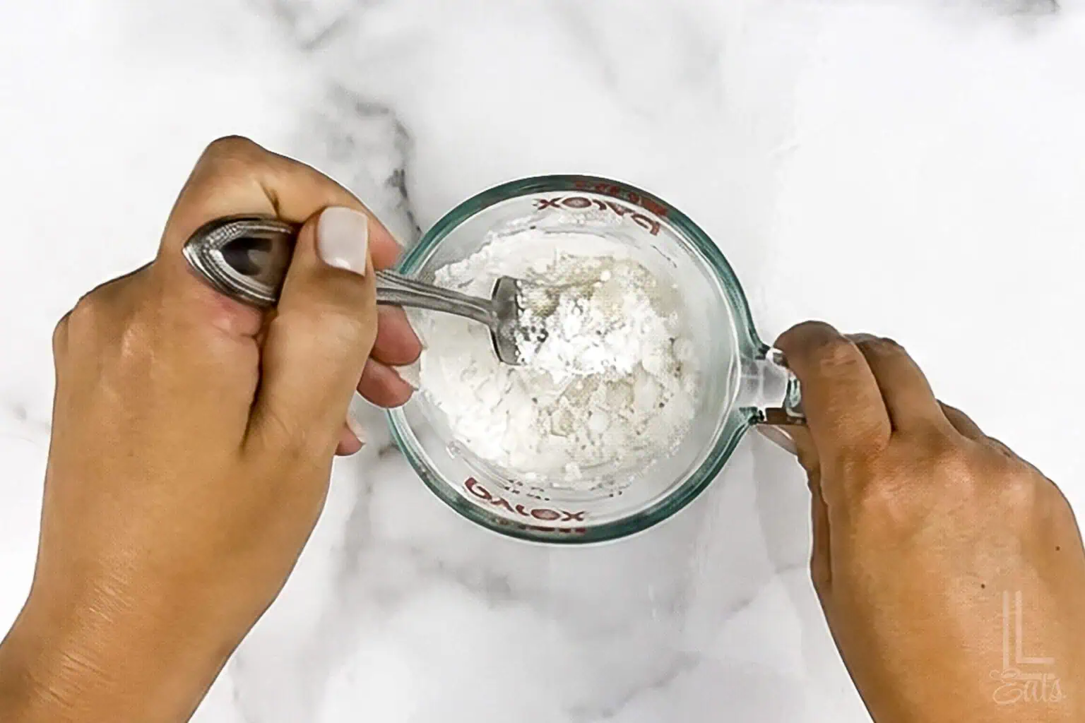 Stirring powdered sugar, half and half, and vanilla in a measuring cup.