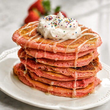 cake mix pancakes stacked on a plate, topped with icing syrup and whipped cream.