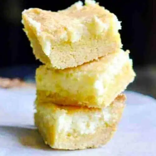 lemon cream cheese bars stacked on a piece of parchment paper.
