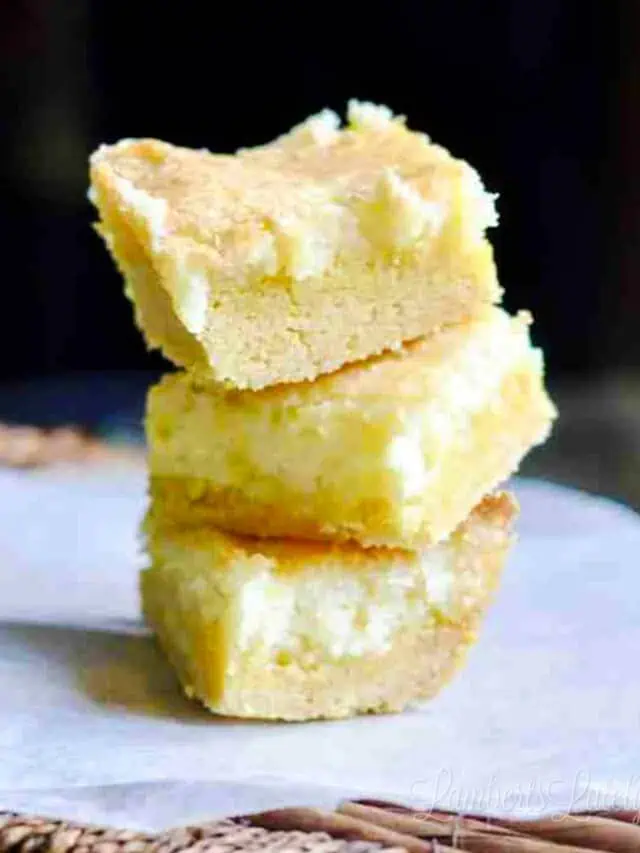 lemon cream cheese bars stacked on a piece of parchment paper.