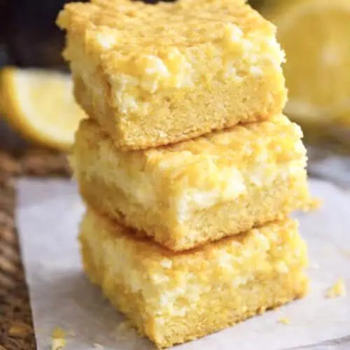 lemon chess bars stacked on a piece of parchment paper.
