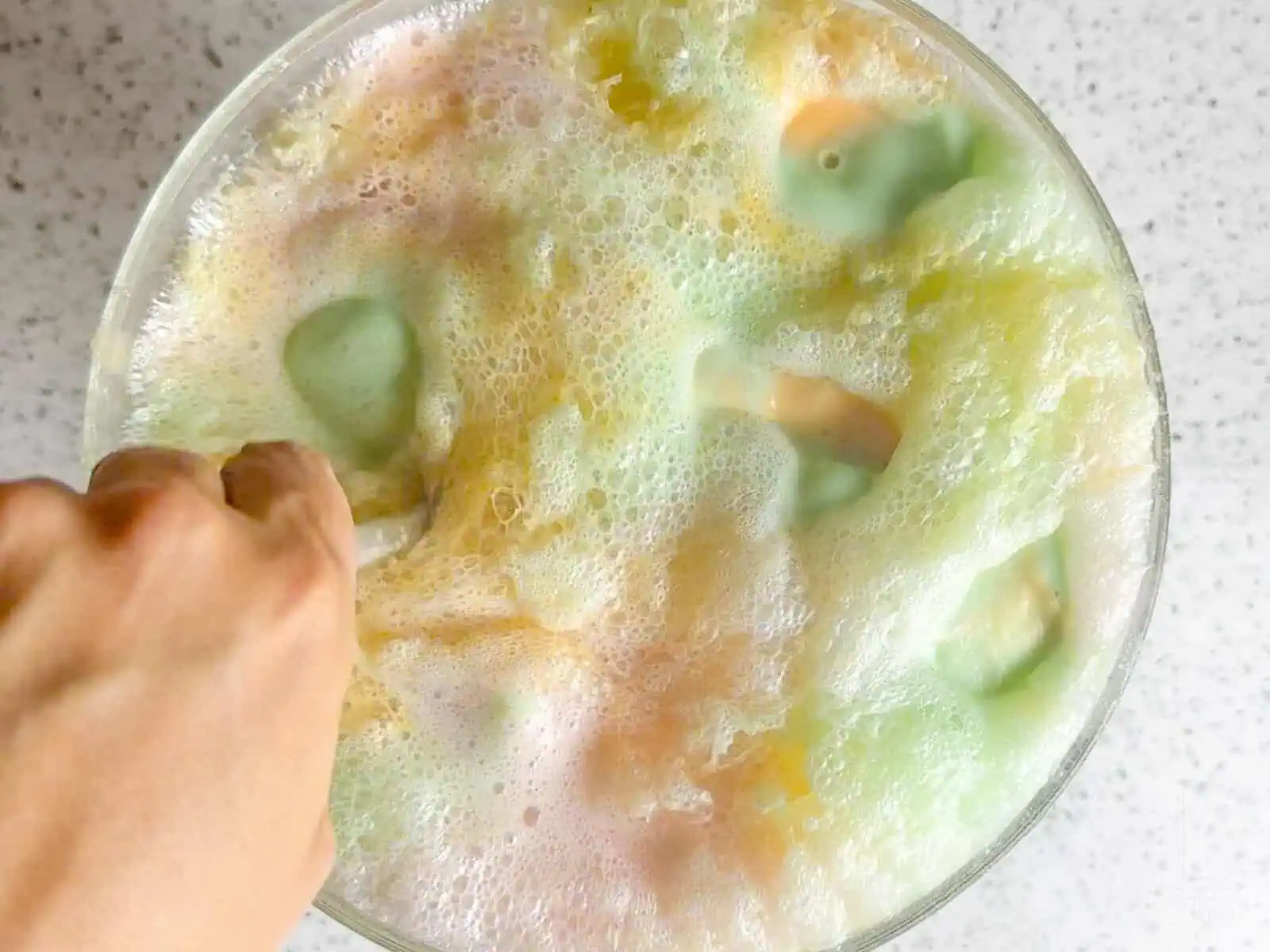 Stirring rainbow sherbet punch in a large bowl as the flavors start to blend.