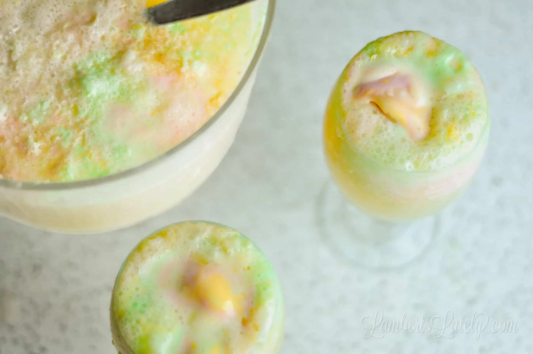 a punch bowl of rainbow sherbet punch with two glasses full of punch.