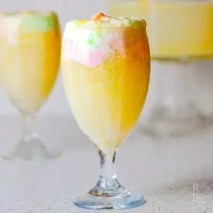 A close-up of a festive glass filled with bubbly rainbow sherbet punch showing the creamy foam top.