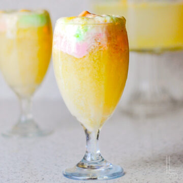 A close-up of a festive glass filled with bubbly rainbow sherbet punch showing the creamy foam top.