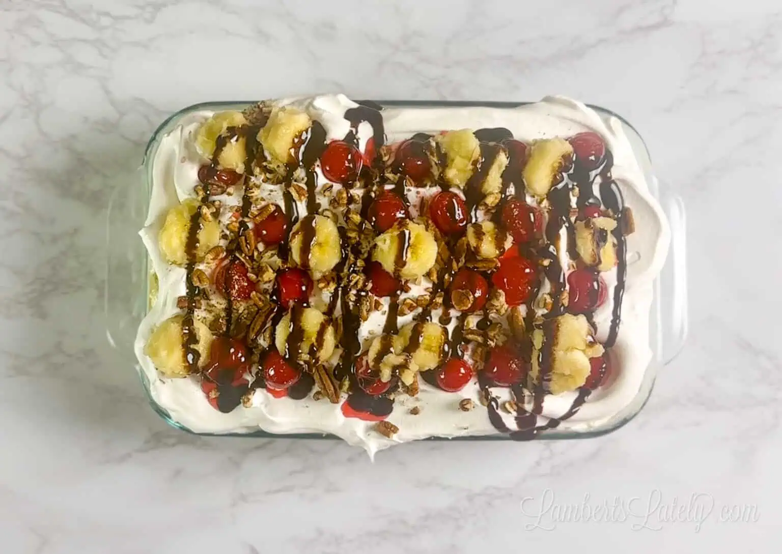 banana split toppings (like whipped topping, bananas, cherries, and chocolate syrup) layered over top of the prepared and chilled banana split cake.