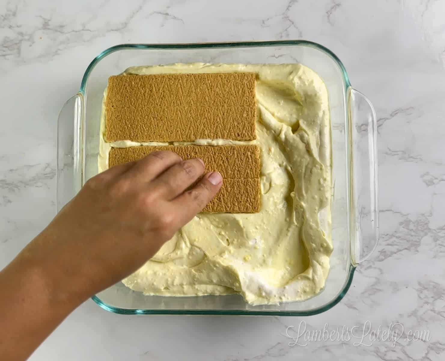 placing graham crackers over pudding mix in a square baking dish.