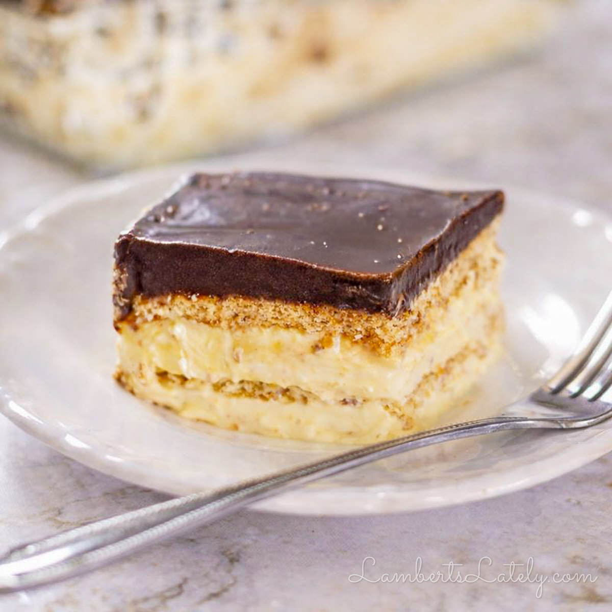 piece of chocolate eclair cake, topped with chocolate ganache, on a plate with a fork.