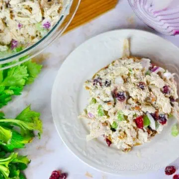 rotisserie chicken salad on a plate, next to bowl of salad and celery.