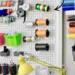 Organized craft room pegboard with spools of thread, tools, and storage bins.
