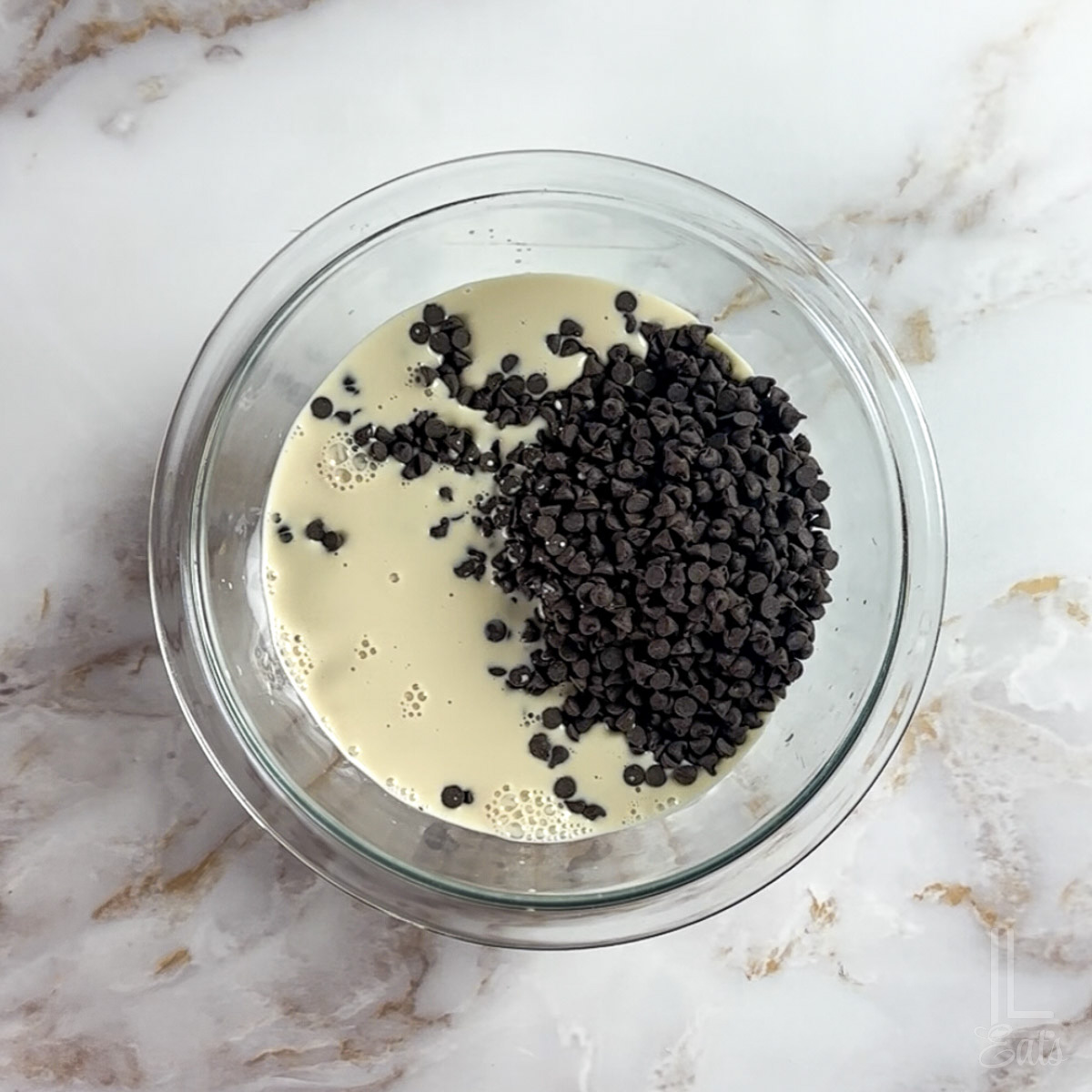 combining semi-sweet chocolate chips and evaporated milk in a glass, microwave-safe bowl.