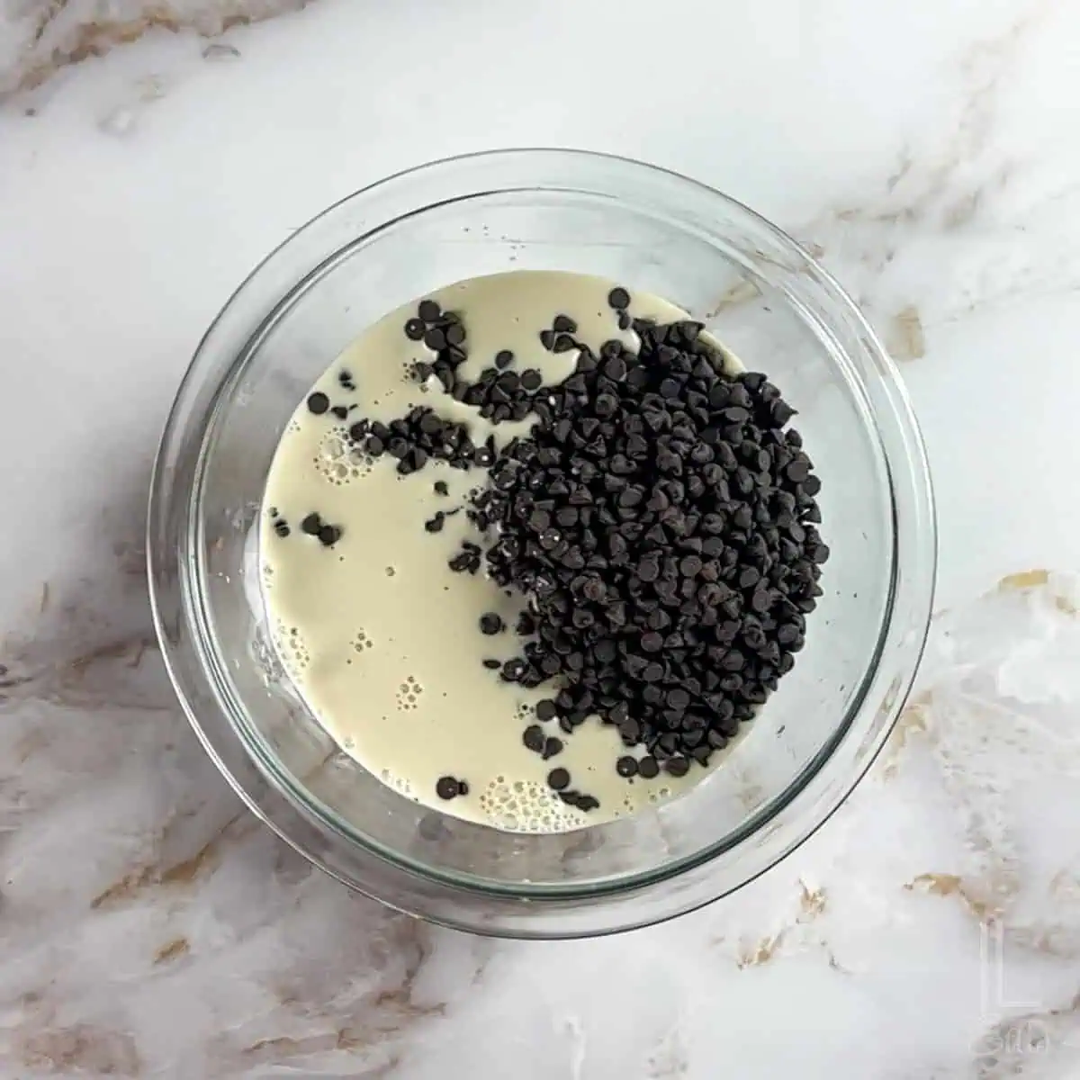 combining semi-sweet chocolate chips and evaporated milk in a glass, microwave-safe bowl.