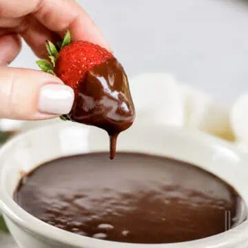 a strawberry half covered in a smooth chocolate dip, above a bowl of the creamy dip.