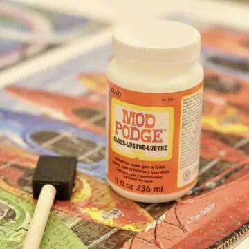 bottle of mod podge and a sponge brush on a finished jigsaw puzzle.