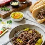 Delicious shredded Italian beef served with peppers and bread rolls on a table.