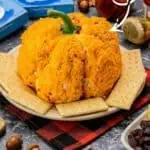 Pumpkin-shaped cheese ball with crackers and festive decorations on a plate.