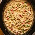 Creamy chicken spaghetti in a black slow cooker with vegetables and herbs.