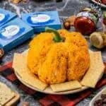 Pumpkin-shaped bacon cheese ball with crackers and fall decorations on a table.