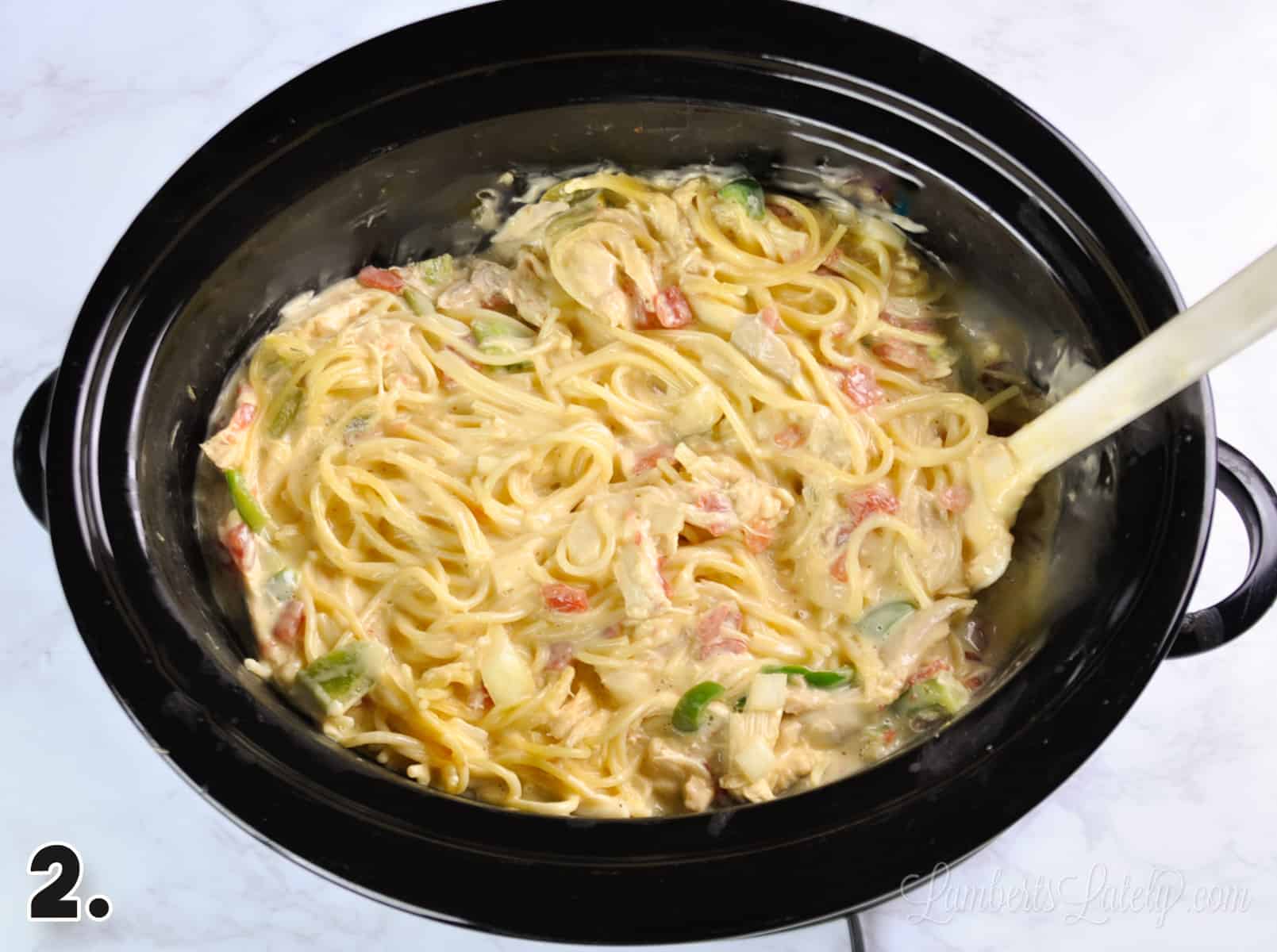 spaghetti noodles added to cheese sauce mixture in a crock pot.