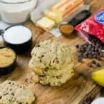 Banana bread cookies with chocolate chips, bananas, and baking ingredients on a wooden surface.