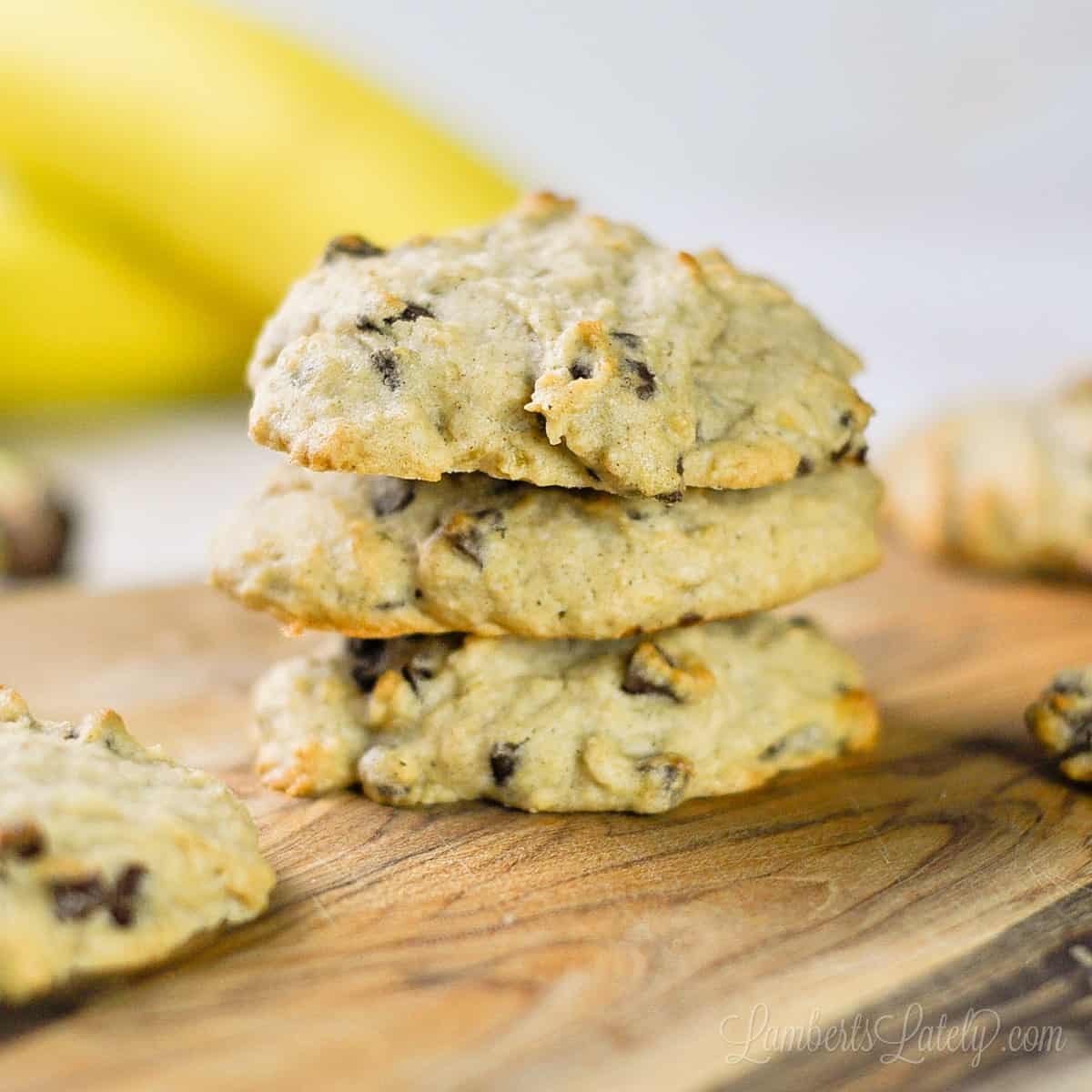 three banana bread chocolate chip cookies stacked on a cutting board.