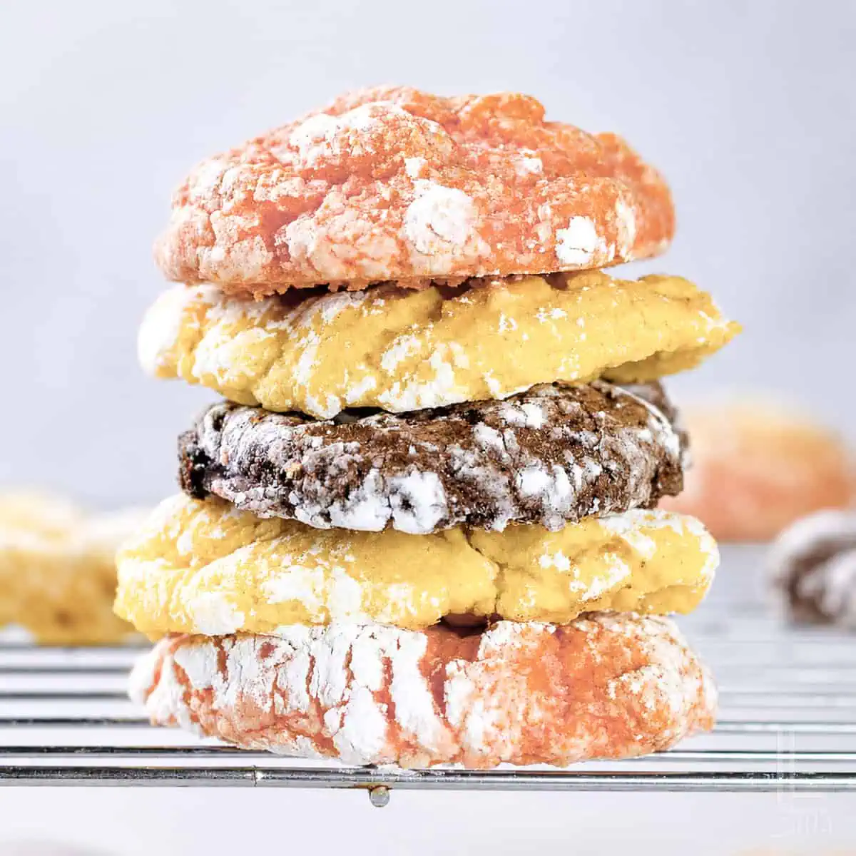Lemon, chocolate, and strawberry Cool Whip cake mix cookies stacked on a cooling rack.