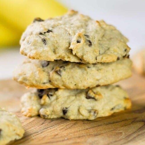 three banana bread chocolate chip cookies stacked on a cutting board.