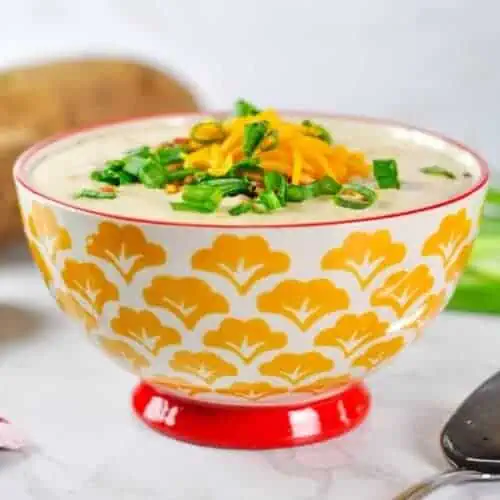 bowl of potato soup topped with cheddar, bacon, and green onions.