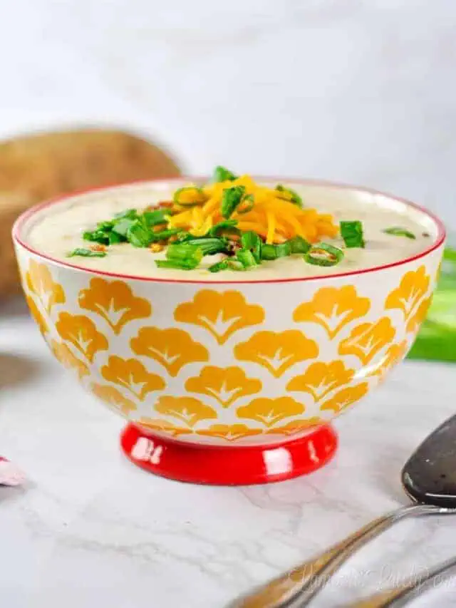 bowl of potato soup topped with cheddar, bacon, and green onions.