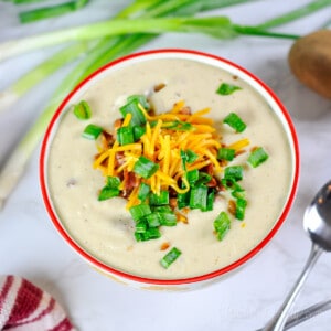 bowl of potato soup with green onions, cheddar cheese, and crumbled bacon on top.