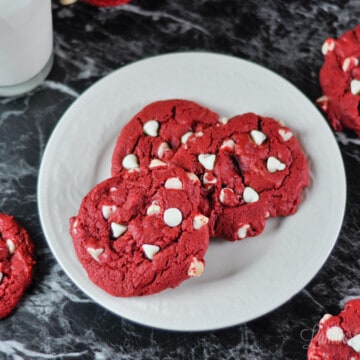 red velvet cookies on a plate, with a glass of milk to the side.