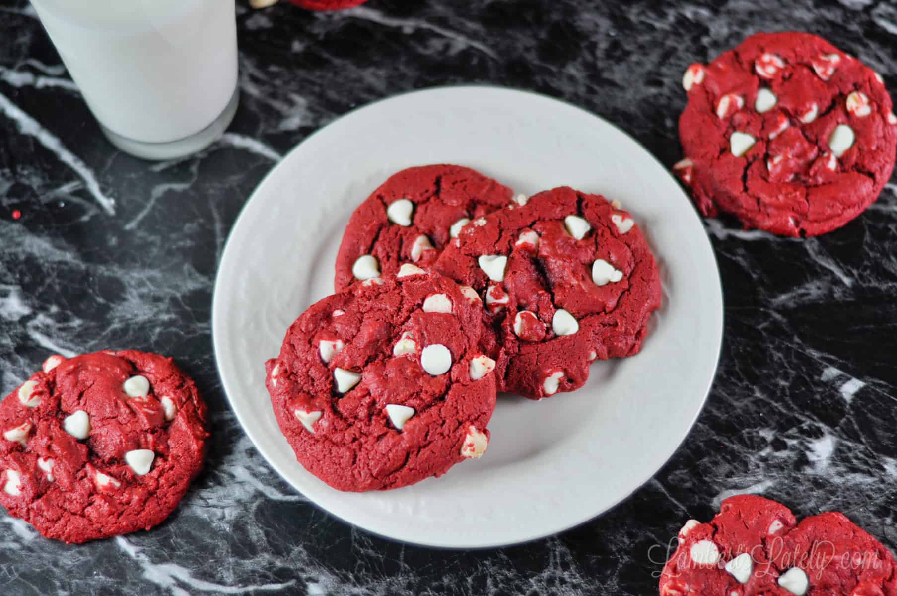 red velvet cookies on a plate, with a glass of milk to the side.