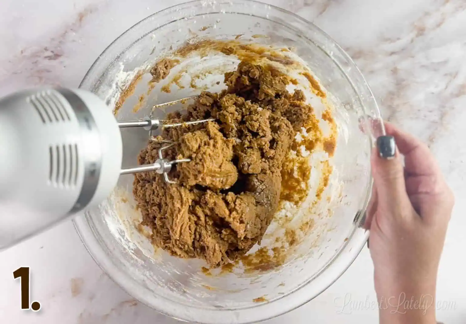 using a hand mixer to blend cookie dough in a glass bowl.