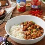Close-up of a bowl of Hoppin' John with rice and seasoned beans, with tomato paste and chili peppers.