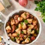 Crispy potato wedges with red potatoes, herbs, and seasonings in a bowl.