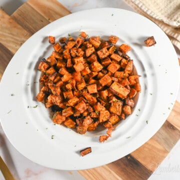 air fryer sweet potato cubes in a bowl on a cutting board, with a fork and a cloth napkin.