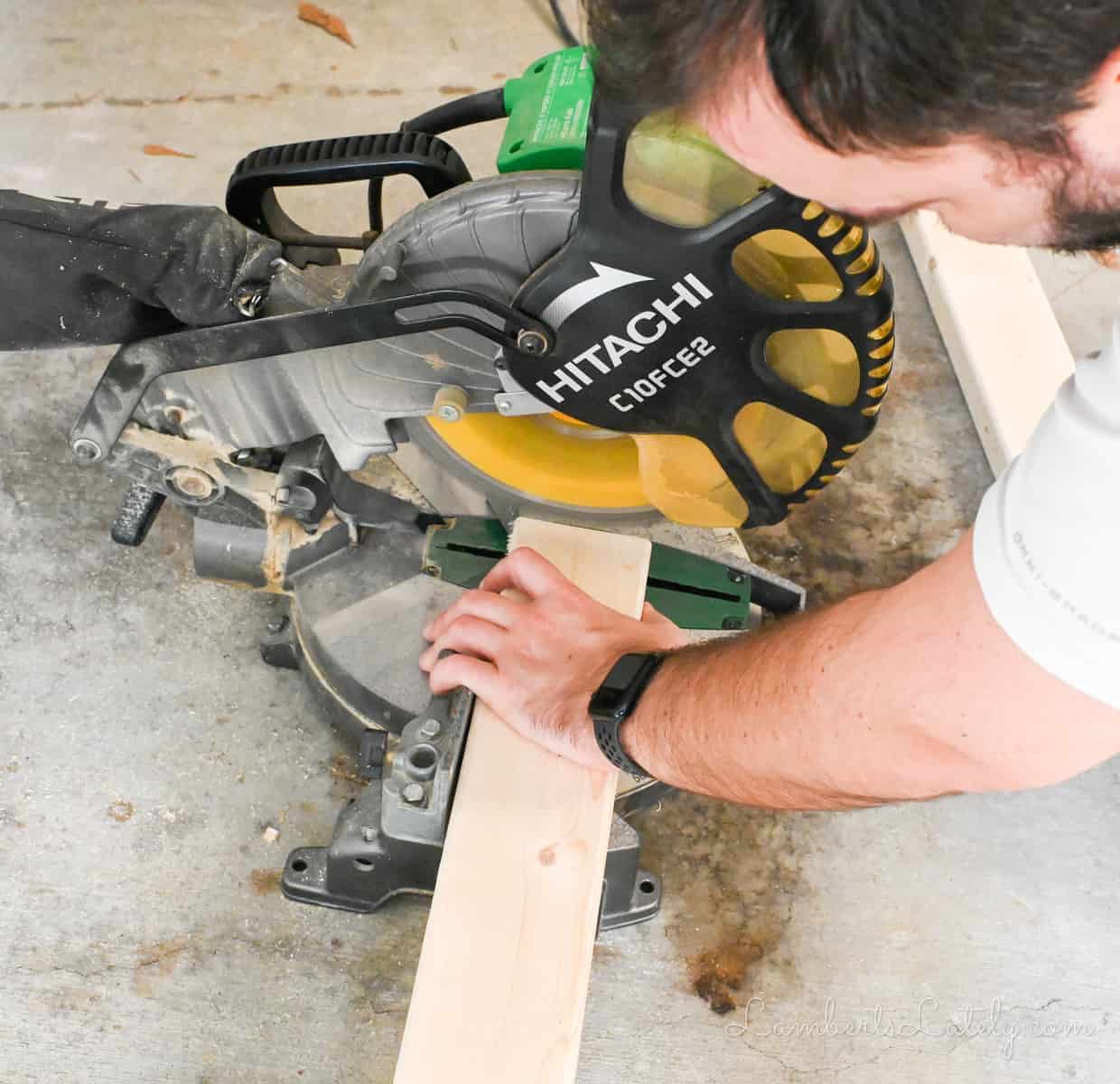 man cutting a piece of wood with a miter saw.